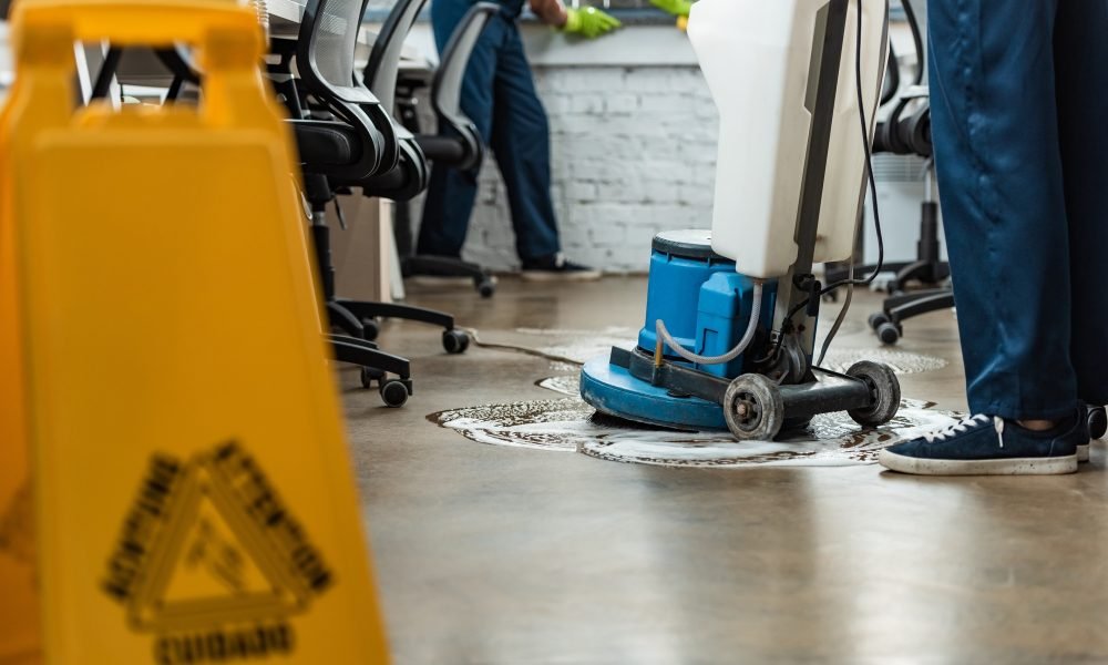 cropped view of cleaner washing floor with cleaning machine near colleague